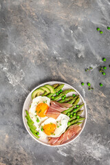 Tasty breakfast. avocado, asparagus, jamon, ham, prosciutto and fried egg on white plate. vertical image. top view. place for text