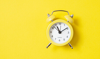 One small alarm clock with a double bell made of yellow metal on a yellow background. Top view and...