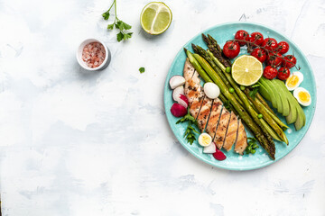 Healthy brunch breakfast with baked asparagus, chicken fillet, cherry tomatoes, avocado, quail eggs and radishes light background. Top view