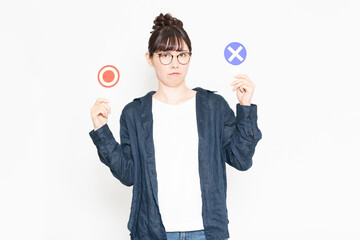 白い背景の前に立ってOKとNGのプラカードを見せる眼鏡をかけている女性