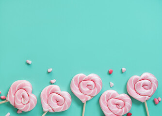 Pink lollipops in the shape of hearts with color sugar on a green background. Top view and copy space