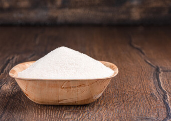 Wooden bowl full of sugar on a wooden background.