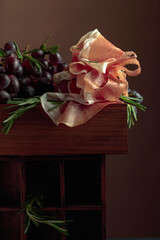 Prosciutto with rosemary and grapes on a brown background..