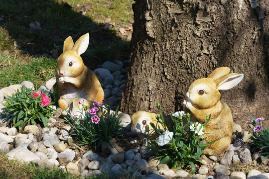 threee easter bunnies in a garden bed in front of a tree trunk