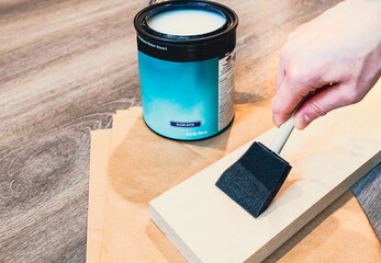 Hand using foam brush testing a clear matte  coating protection paint on sample of birch wood...