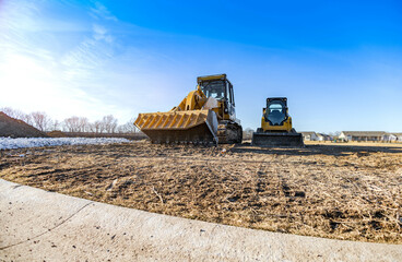 Track bulldozer, earth-moving equipment at construction site with bright blue sky background. Land clearing, grading, ground excavation, foundation digging of large job of new residential building.