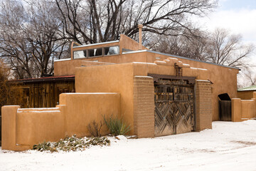 Naklejka premium Traditional adobe building with southwest style wooden door seen from a street covered in rare fresh snow during an overcast winter day, Santa Fe, New Mexico, USA