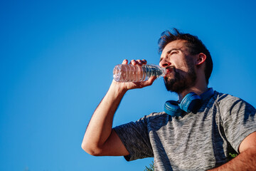 bearded man drinking water on a sunny day over blue sky background