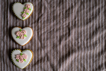 Fototapeta premium White gingerbread cookies with icing and flower decoration on a striped towel. Background for International Women's Day or Valentine's Day. High quality photo