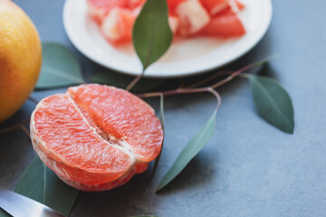 Half a fresh, juicy grapefruit, sliced grapefruit on a plate and a whole grapefruit on a dark marble background with leaves. Citrus fruits is immune boosting food. Healthy organic season fruits
