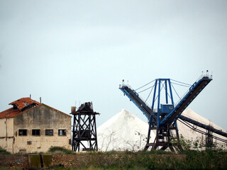 Fototapeta na wymiar Sea salt mining facility, equipment and conveyor, mountains of sea salt
