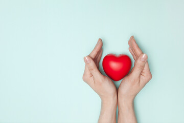 Health, medicine and charity concept - close up of female hands with small red heart