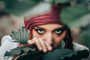 Fototapeta premium Portrait of young female in pirate costume peaking through branches