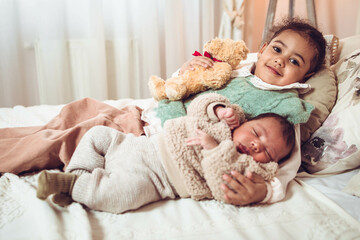 Little multiethnic girl, sister lying next to her baby brother on the bed