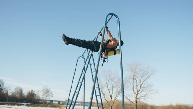 Muscular man with a naked torso is training in a winter park and doing exercise corner and plank on a horizontal bar