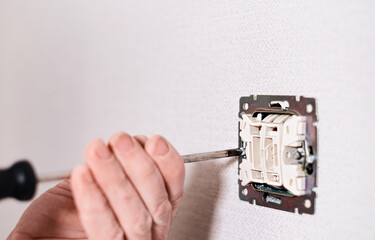 Hands an electrician installing an electrical network in a new house. Assembly of the electrical network in the room. Electrician installing light switch in home.