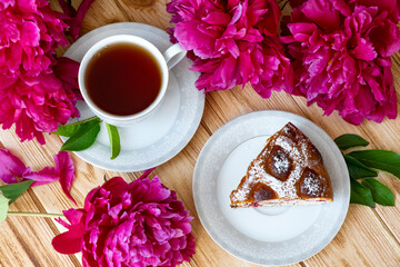 Floral tea time with piece of fresh baked berry pie, cup of tea and lush dark pink peony flowers. Morning breakfast with fresh pastry and floral tea. Flat lay, top view. © Тетяна Немировська