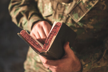 Soldier dressed in camouflage uniform holding a bible in his hand. Soldier reading and meditating on God's word - 494761371