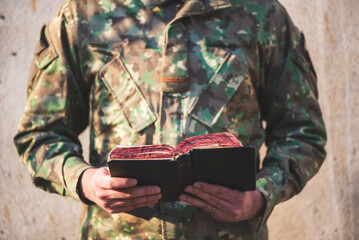 Soldier dressed in camouflage uniform holding a bible in his hand. Soldier reading and meditating on God's word