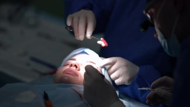 Close-up young Caucasian woman on surgery bed with eyelid dissection and professional plastic surgeon performing operation. Portrait of female patient talking to doctor in operating room. Slow motion