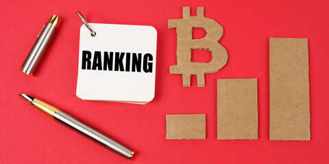 On a red surface lie the bitcoin symbol, a pen and a notepad with the inscription - RANKING
