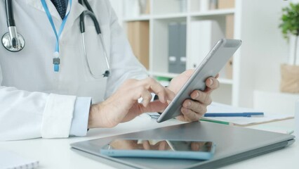 Close-up of male hand in medical uniform using tablet touching screen in hospital office while doctor is working with medical records online