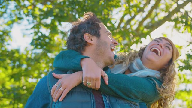 Happy loving couple laughing as man gives woman piggyback ride  in autumn park - shot in slow motion 