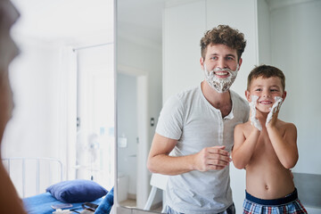 Am I doing it right Dad. Shot of a father teaching his little son how to shave in the bathroom at...