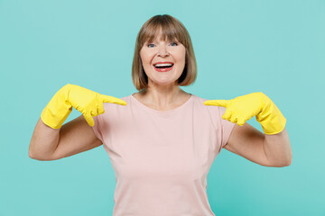 Elderly exultant happy housewife woman 50s in pink t-shirt gloves doing housework point index finger on herself isolated on plain pastel light blue background Housekeeping cleaning tidying up concept.