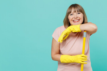 Elderly smiling happy cheerful housewife woman 50s in pink t-shirt gloves doing housework leaning...