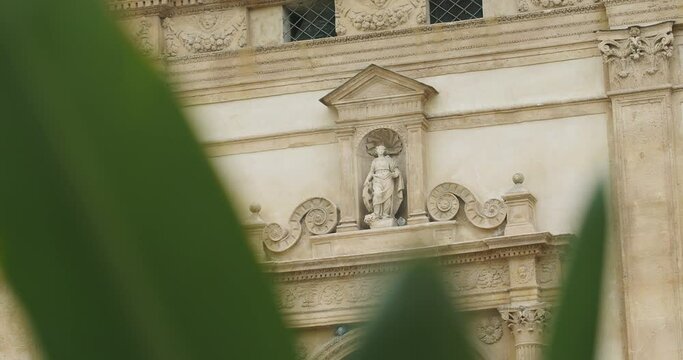 a statue on the arch of the gates of the doors of a large historical building in the rococo style, in the foreground a green leafy cactus flower. motion. close-up