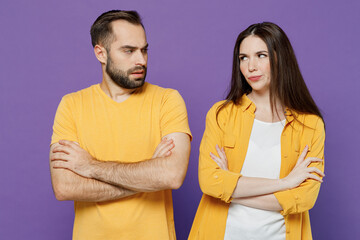 Young sad offended displeased couple two friends family man woman together in yellow casual clothes look to each other hold hands crossed folded isolated on plain violet background studio portrait.