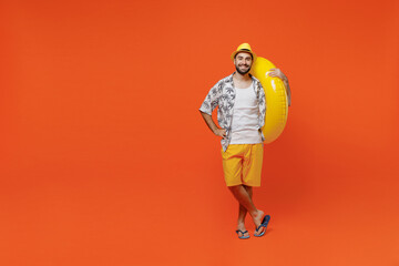 Full body young smiling cheerful cool tourist man wear beach shirt hat hold inflatable ring look camera isolated on plain orange background studio portrait Summer vacation sea rest sun tan concept.