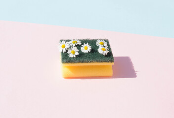 Dishwashing sponge with daisy spring flowers on a pink and blue background. Surreal grass and flower concept. © Bozena Milosevic