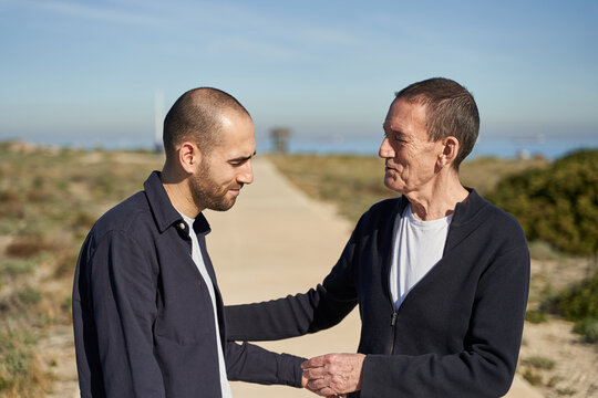 Father and son talking and smiling in sand path near beach