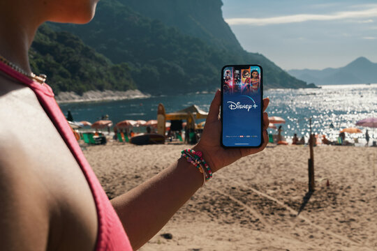 Girl on the beach holding a smartphone with Disney+ (Disney Plus) app on the screen. Rio de Janeiro, RJ, Brazil. March 2022