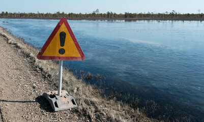warning sign, attention. road next to the reservoir in the spring