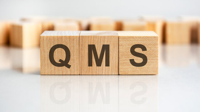 QMS - letters on wooden cubes. business as usual concept image. front view
