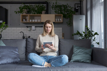 Woman sitting on sofa at home, using tablet computer, reading e-books and online learning