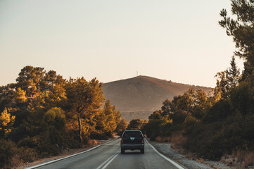 A pick up truck driving on a n asphalt road going through rocks and trees in the countryside of Rhodes, Greece