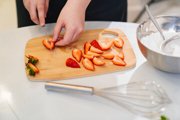 strawberries are cut into pieces on a wooden cutting board to decorate desserts.