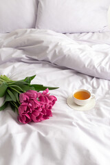 Bouquet of pink tulips and cup of tea on bed with lilac linen.
