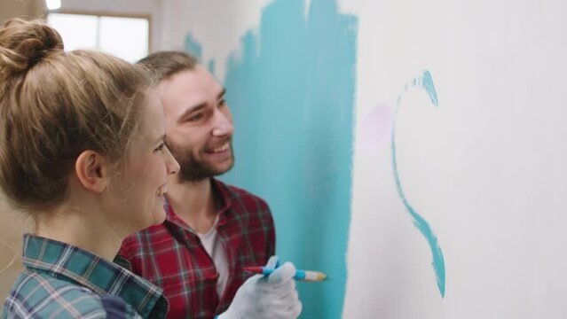 Taking video closeup of a beautiful young couple Caucasian looking painting together a big hart in their living room wall they enjoy the moment at home