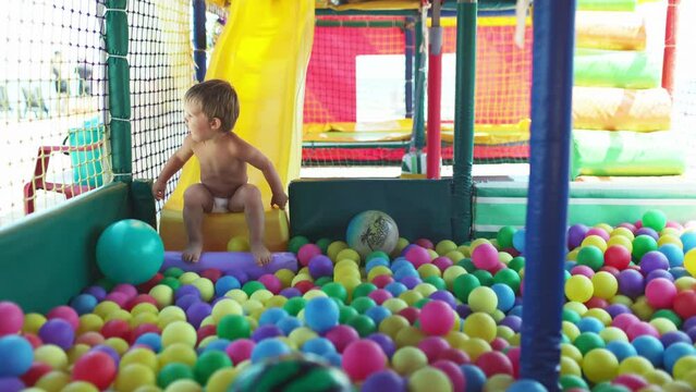 The kid plays in the playroom and rolls down the slide into the pool with small balls
