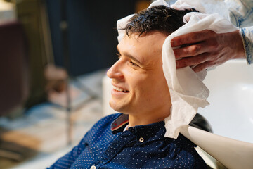 hairdresser wipes hair of brunette man with disposable towel after washing hair