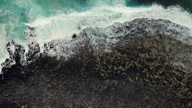 Aerial view breaking waves of Atlantic Ocean, rocky beach, black volcanic stones, bay with turquoise water directly above view, nature background. No people. Lanzarote, Canary Islands, Haria. Spain
