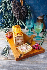 Traditional French Pate en croute with rabbit meat and pork filet serviert with grapes as close-up on a modern design wooden board