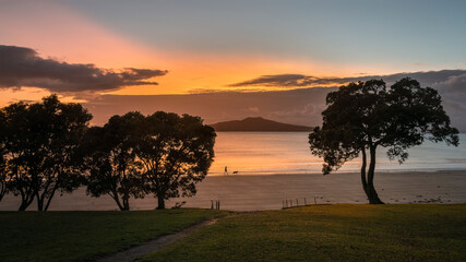People and dog walking at Takapuna beach at sunrise. Rangitoto Island in the background, Auckland.