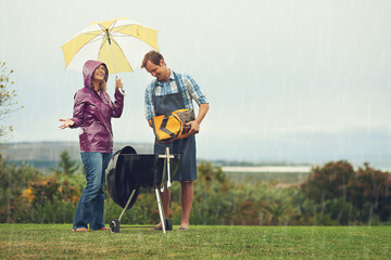 We barbecue anytime, anywhere. Shot of a couple happily barbecuing in the rain.