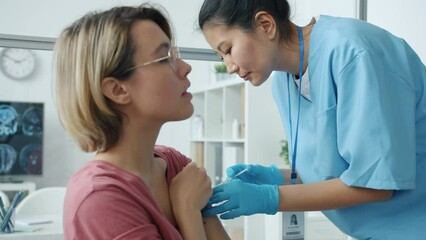 Nurse in uniform giving covid-19 vaccine injection to serious young lady in hospital room. Corona virus pandemic and vaccination concept. - Powered by Adobe